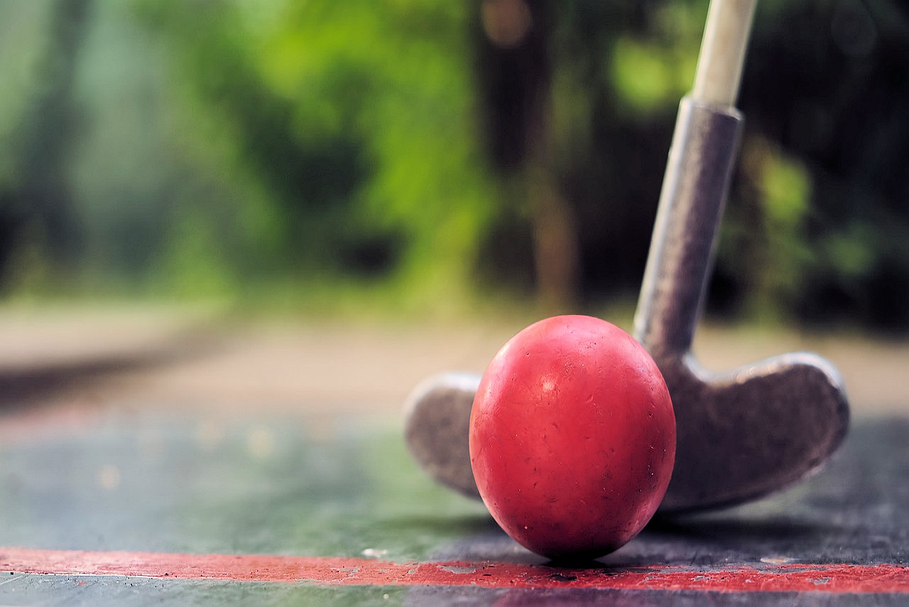 A mini golf club about to hit a golf ball on a sunny day