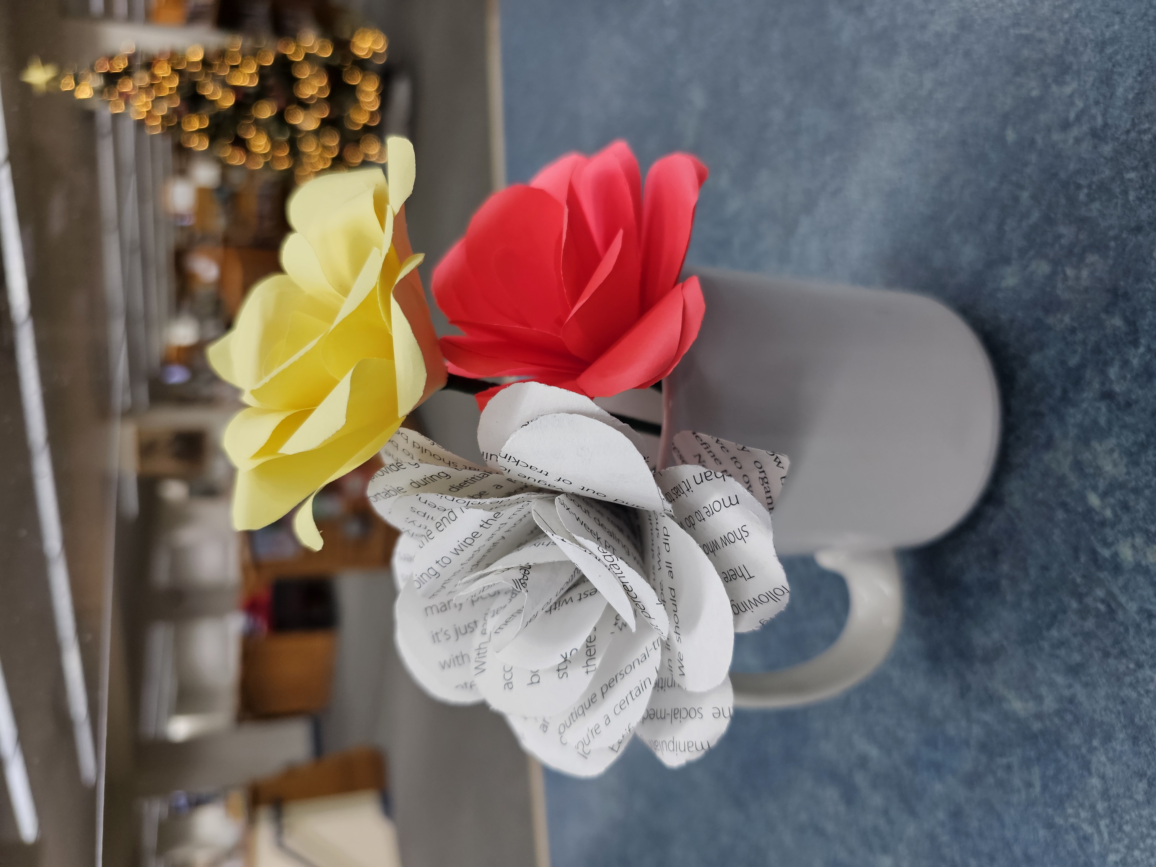 White cup sitting on blue table with paper roses inside