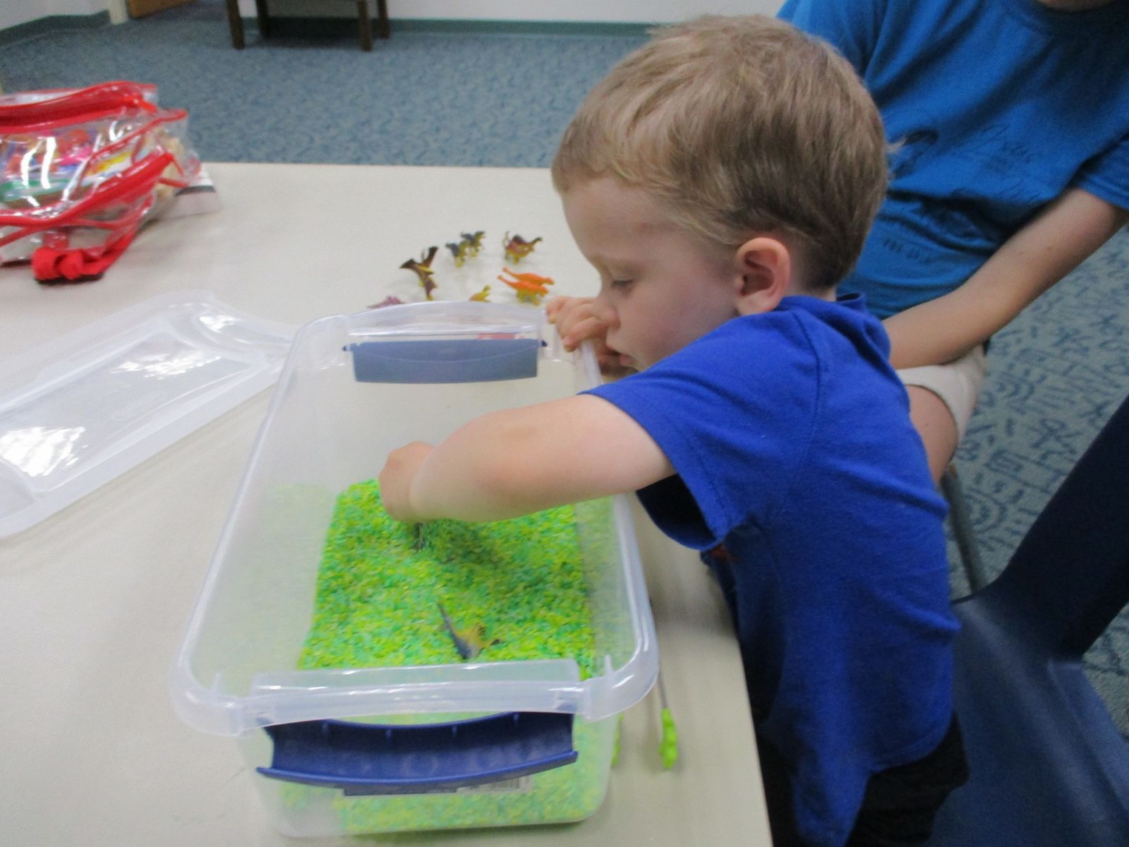 A boy digs for toys in a sensory bin of green rice.