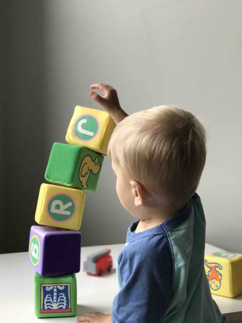 A young child stacks a series of soft toy blocks.