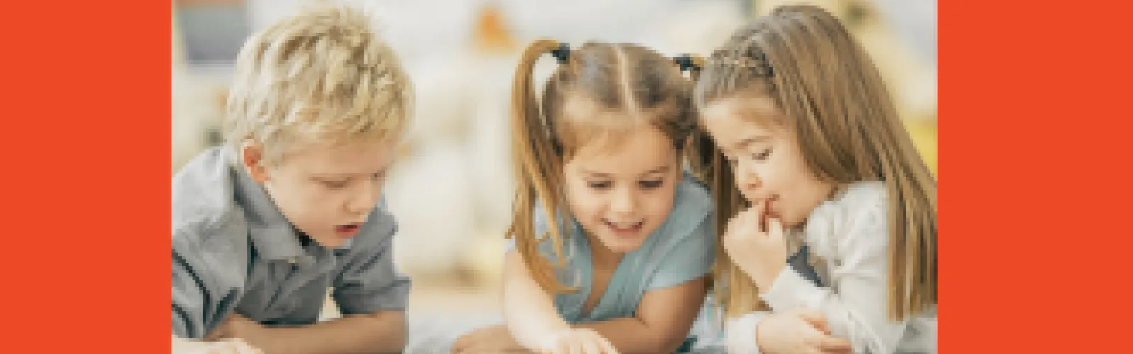 Three children lying on the floor, happily reading a book together.